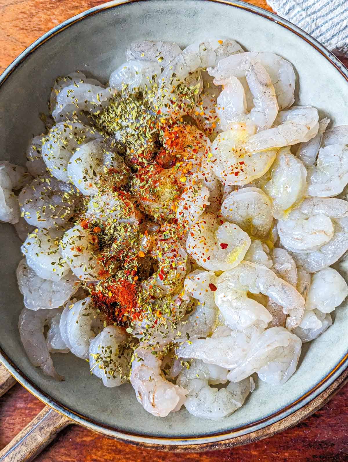 The raw shrimp in a bowl with seasoning and butter sprinkled on top.