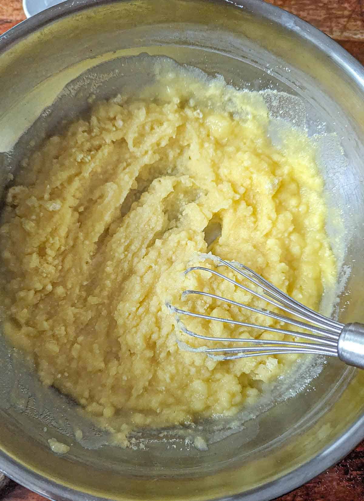 Whisking the cornmeal into the simmering water in a saucepan.