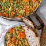 Romanian green pea stew served in a bowl with bread.