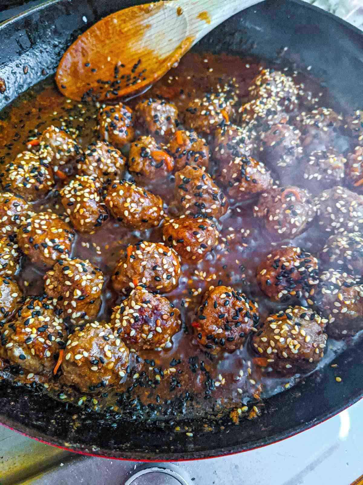 adding sauce to hoisin meatballs cooking in a skillet