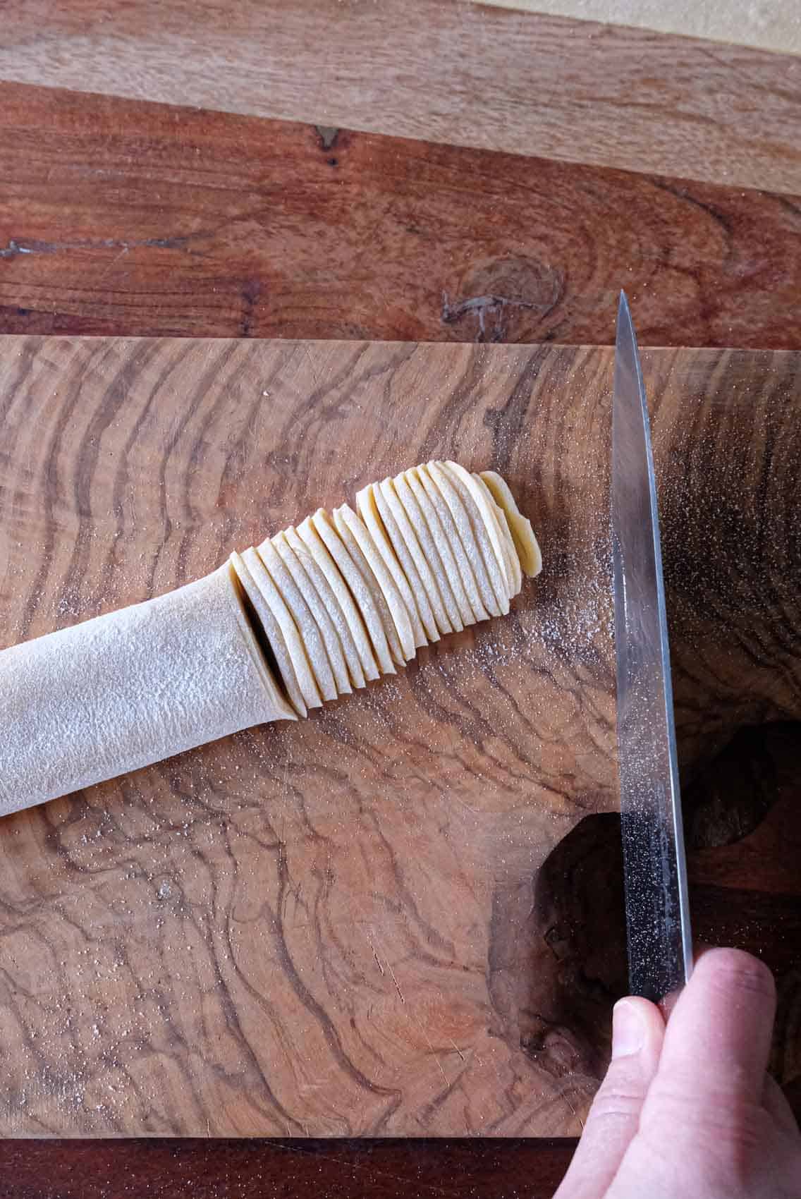 Thinly slicing a sheet of rolled pasta dough to make spaghetti.