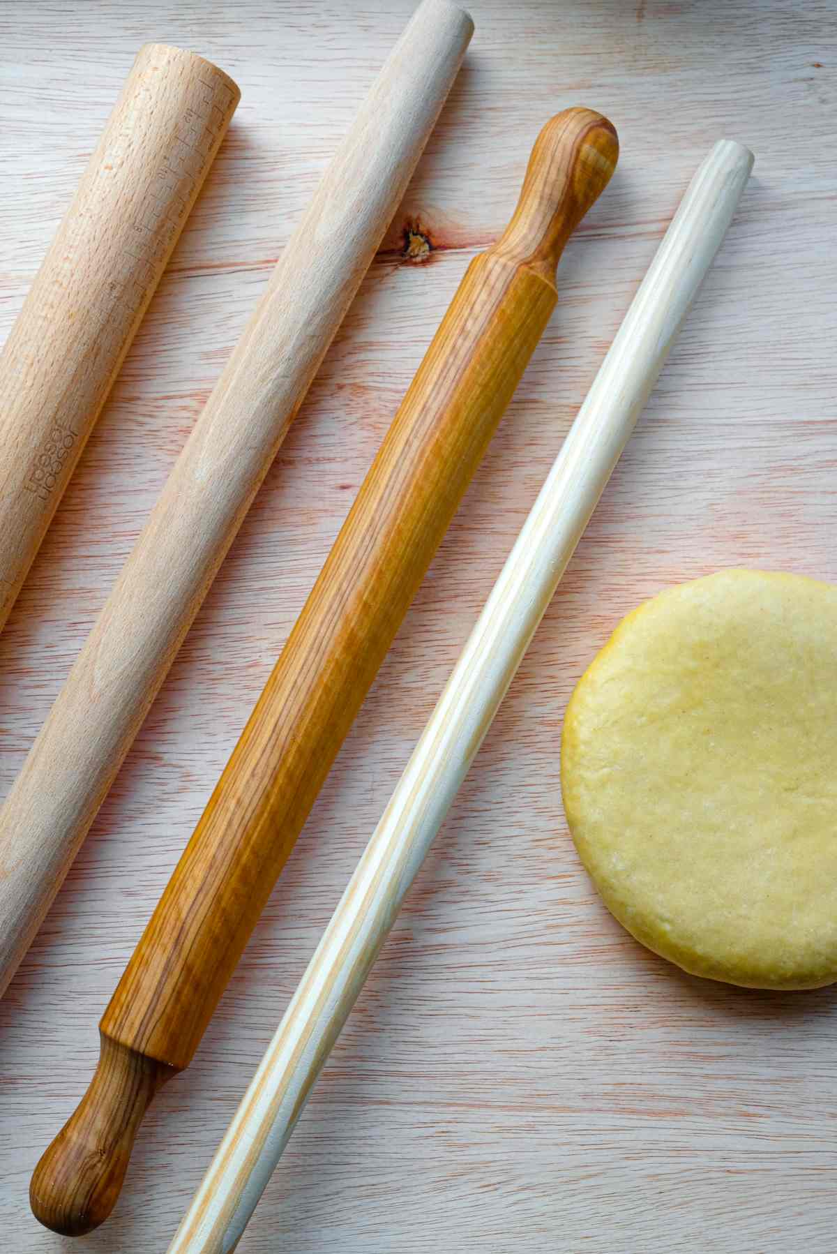 Different types of rolling pins beside a ball of pasta dough.