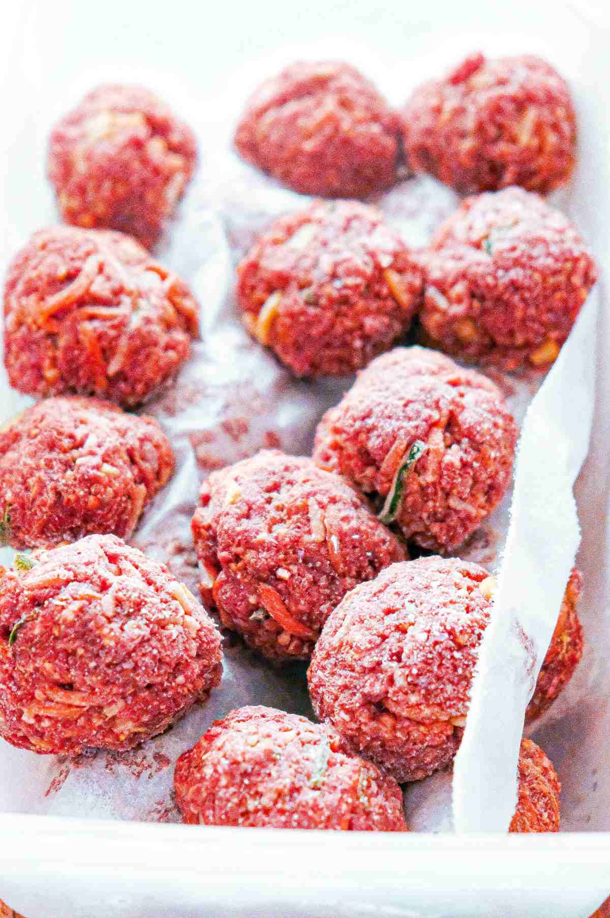 Frozen meatballs between layers of parchment paper in a tupperware container.