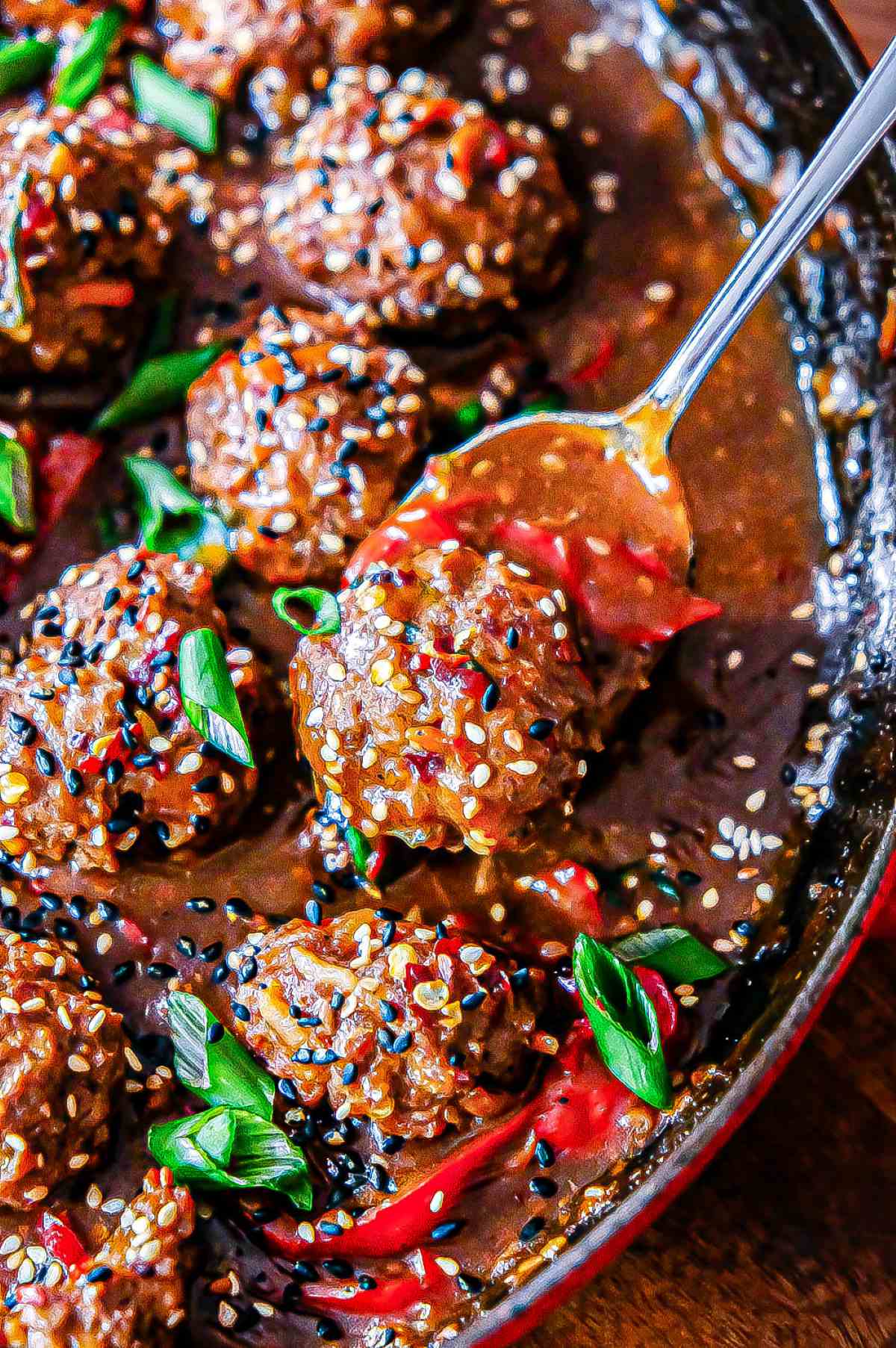 Hoisin meatballs in a skillet in sauce with sesame seeds and sliced green onions.