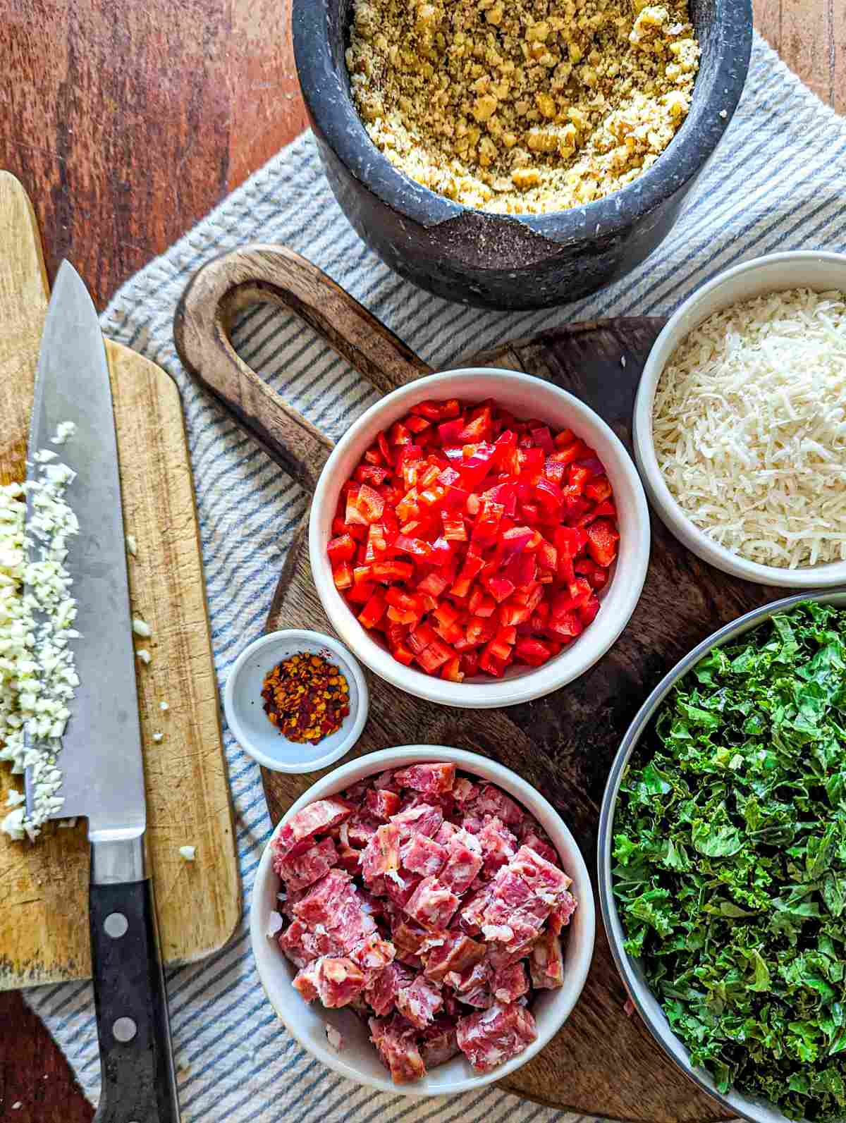 Ingredients for rigatoni pasta including crumbled walnuts, parmesan, red pepper, kale, smoked sausage, and garlic.