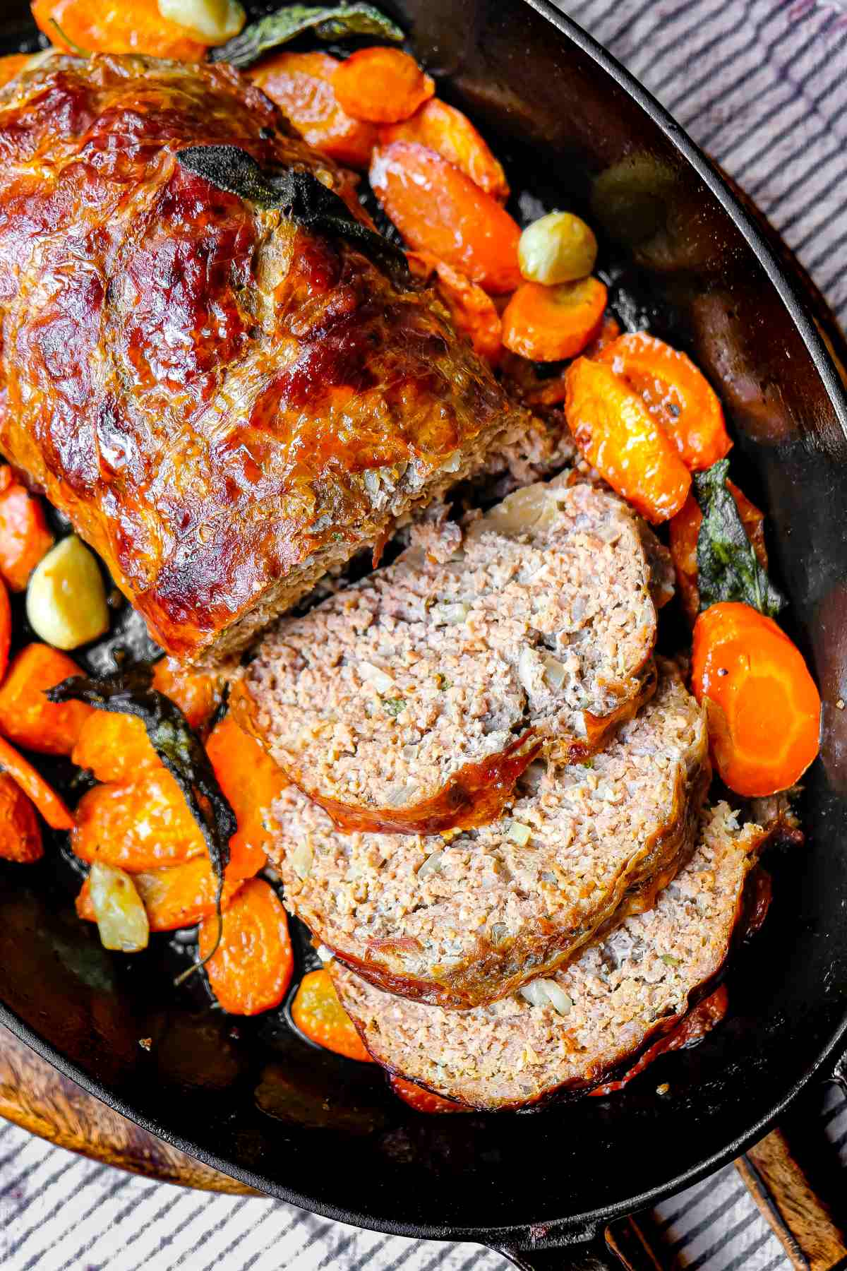 sliced prosciutto covered meatloaf with carrots in roasting pan after cooking