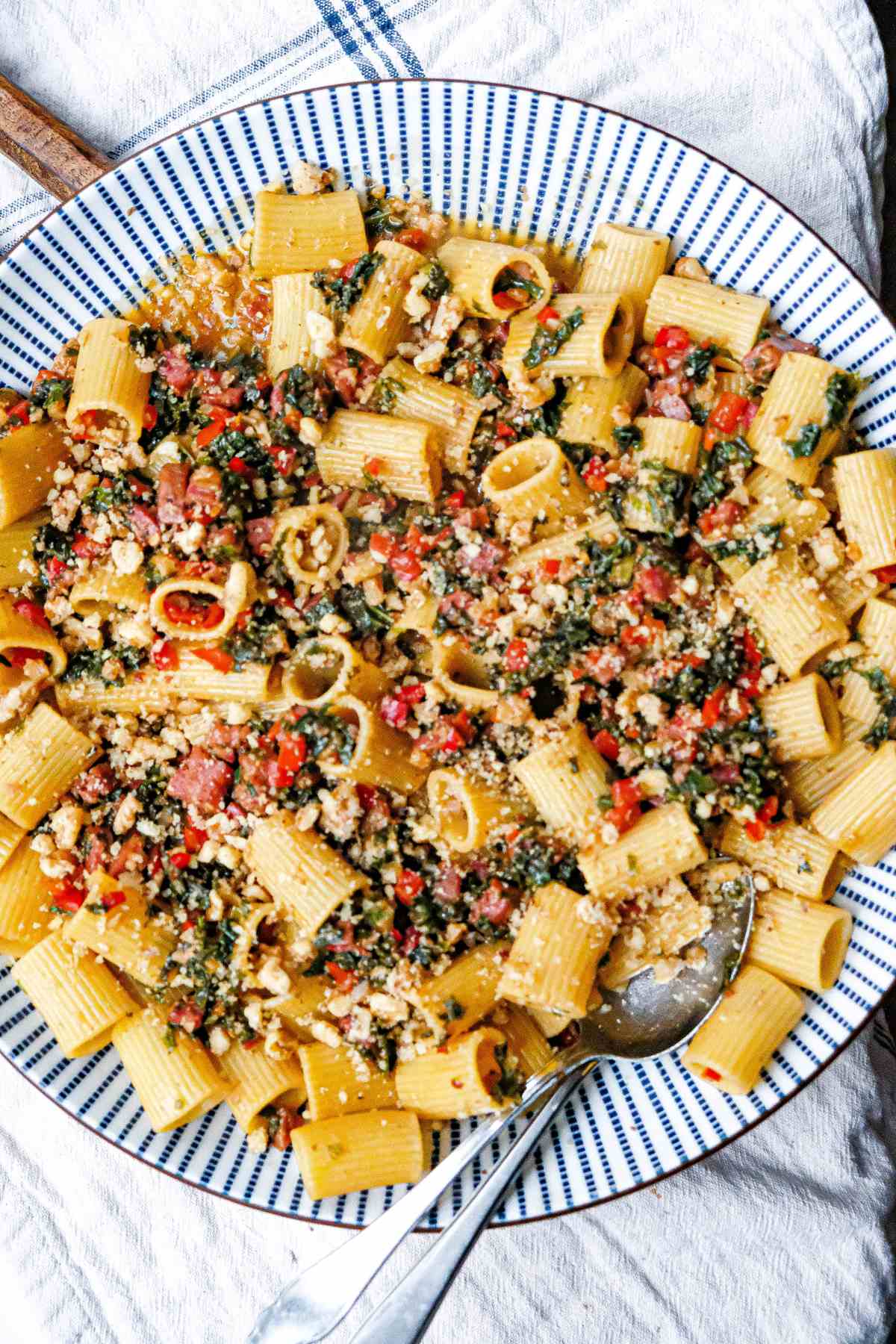 A plate of rigatoni pasta with smoked sausage, kale, red pepper and walnut crumble.