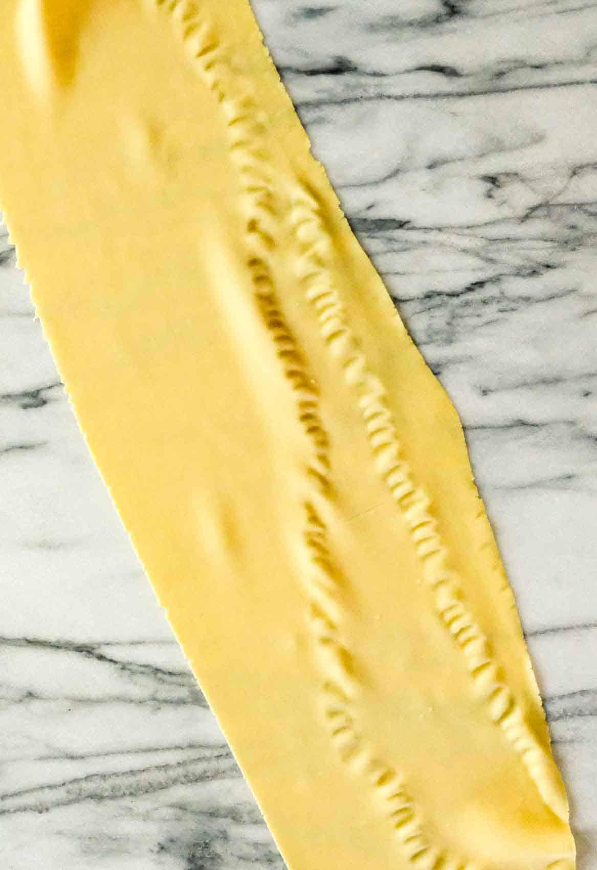 Pasta dough rolled out with a machine showing crimping from pressing a piece of dough that is too wide.