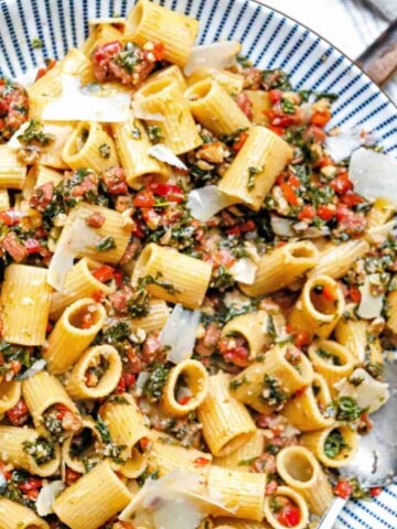 A plate of rigatoni pasta with smoked sausage, kale, red pepper and walnut crumble.