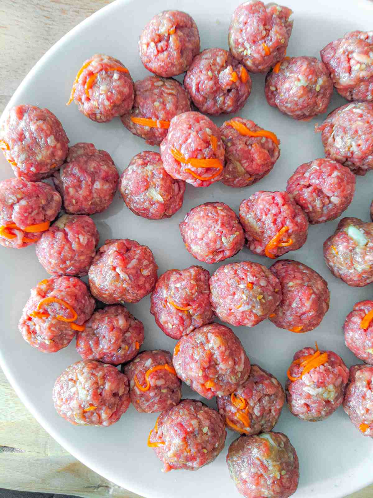 A plate full of uncooked meatballs ready to be frozen or fried.