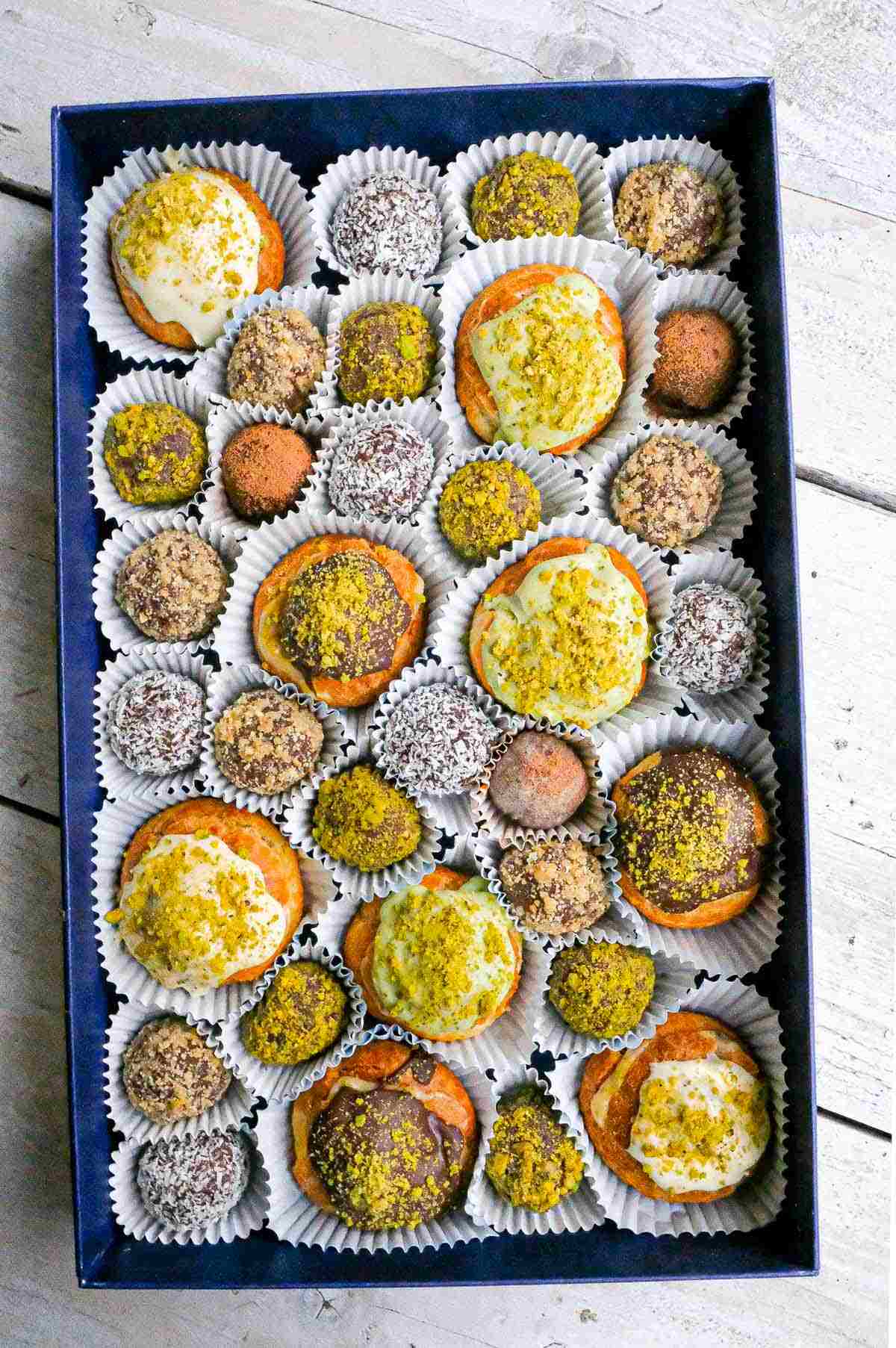 A box of multicolored Christmas rum balls with coconut, cocoa powder, pistachio, and walnut.