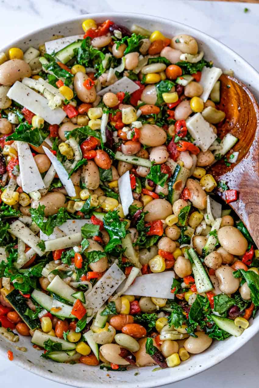 A larger bowl full of bean salad being stirred by a large wooden spoon.