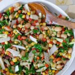 A larger bowl full of bean salad being stirred by a large wooden spoon.