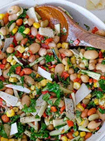 A larger bowl full of bean salad being stirred by a large wooden spoon.