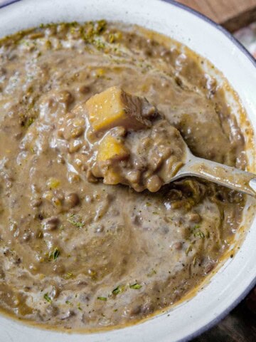 a bowl of lentil potato soup with a spoon it it showing the texture of the soup